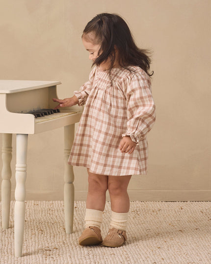 A toddler wearing a long-sleeve smocked dress with a rustic plaid pattern