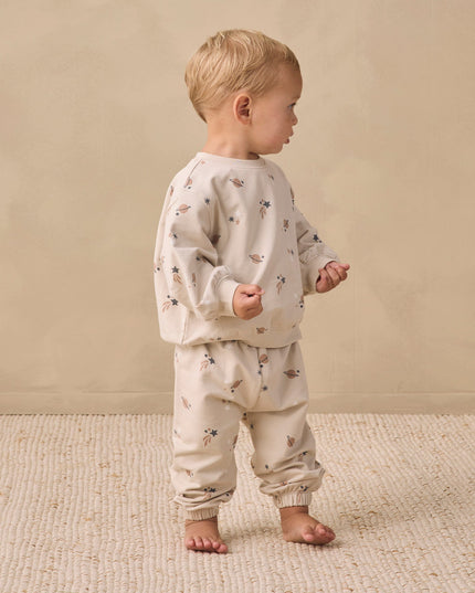 A boy wearing a matching sweatshirt and sweatpants with an all over space print. 