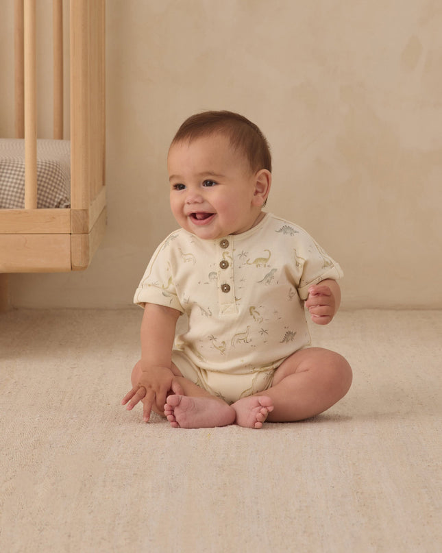 Baby sitting on floor in nursery wearing dinosaur romper