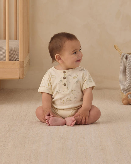 Baby sitting on floor in nursery wearing dinosaur romper