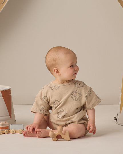 Baby wearing beige romper with lion print