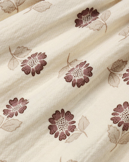 A close-up of a cream-colored dress with a muted purple flower pattern