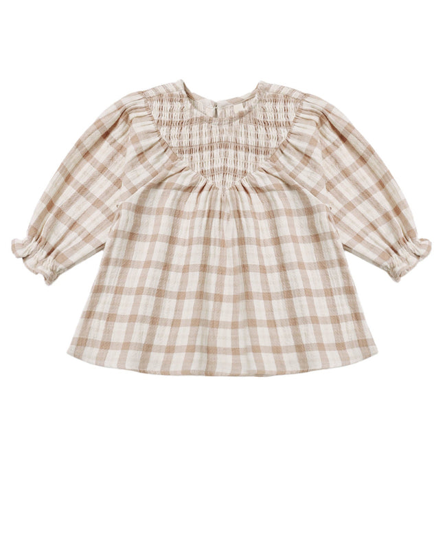 A toddler girl's long-sleeve dress in a beige and white gingham plaid pattern, featuring a smocked bodice, ruffled collar, and ruffled cuffs.