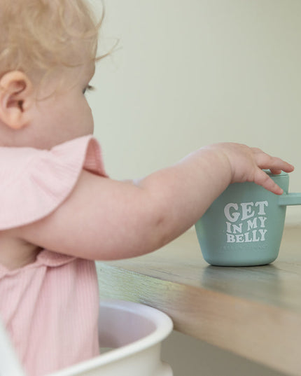 Baby reaching for light green snack container with handles and text 'Get in my belly' 