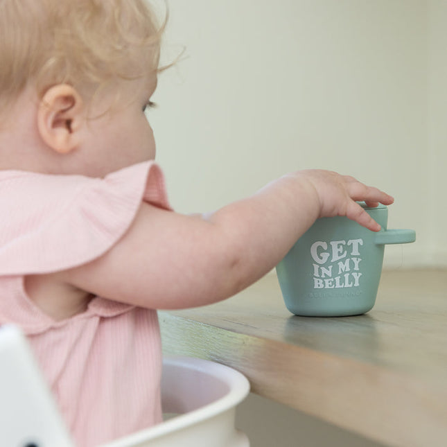 Baby reaching for light green snack container with handles and text 'Get in my belly' 