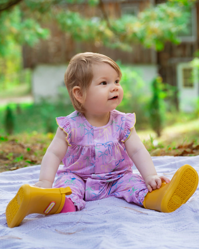 Baby wearing purple bow pattern romper with ruffle sleeves and magnetic closure