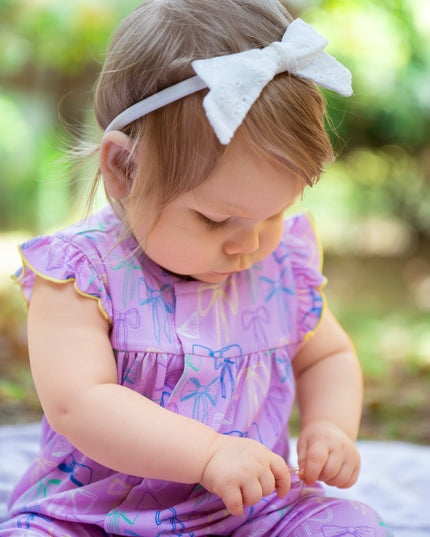 Baby wearing purple bow pattern romper with ruffle sleeves and magnetic closure