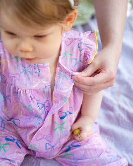 Baby wearing purple bow pattern romper with ruffle sleeves and magnetic closure