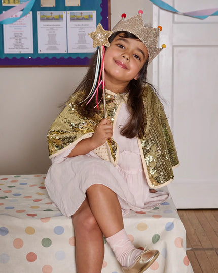Girl dressed wearing a flitter cape, crow and holding a star wand