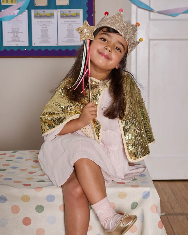 Girl dressed wearing a flitter cape, crow and holding a star wand