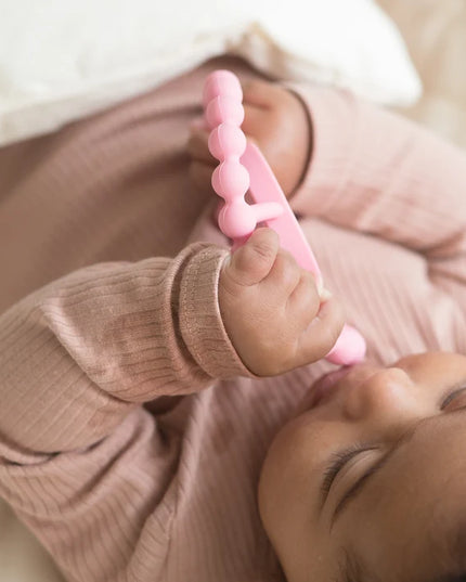 A baby chewing on a pink silicone baby teether 