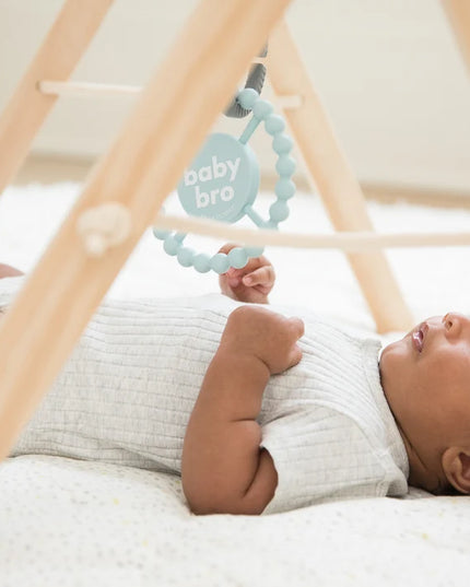Baby playing with light blue silicone baby teether with the text 'baby bro'