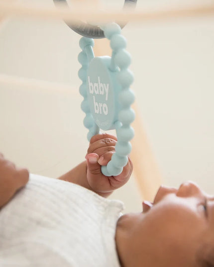 Baby playing with light blue silicone baby teether with the text 'baby bro'