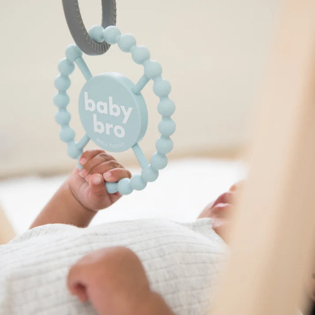 Baby playing with light blue silicone baby teether with the text 'baby bro'
