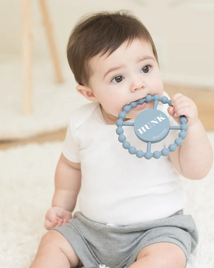 Baby holding a blue teething ring with 'HUNK' text