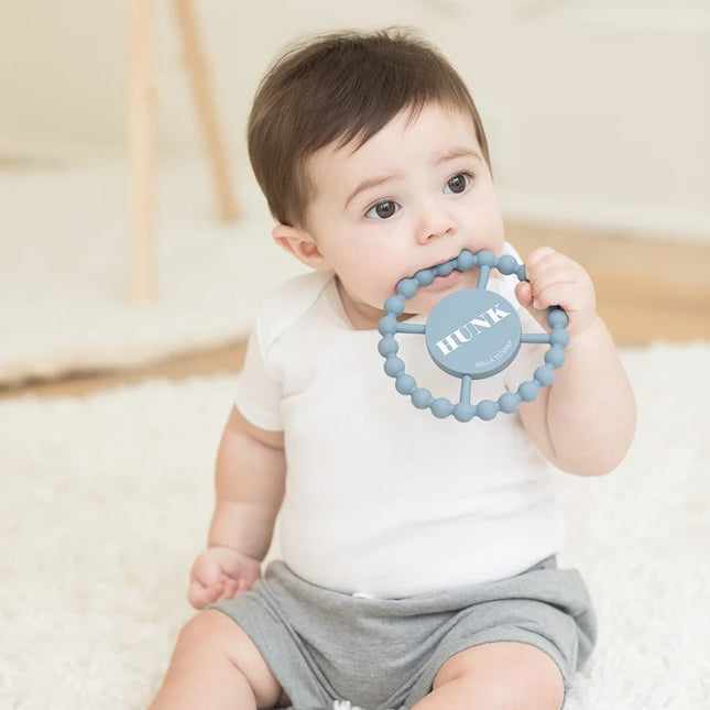Baby holding a blue teething ring with 'HUNK' text