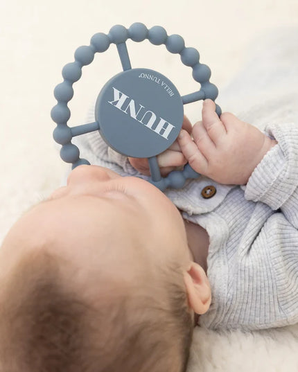 Baby holding a blue teething ring with 'HUNK' text