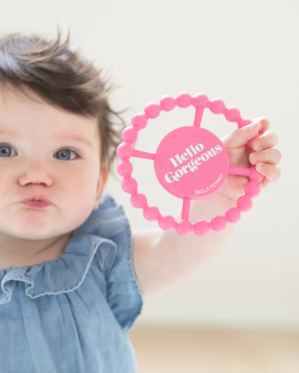 Baby holding pink silicone teething ring with 'hello gorgeous' text