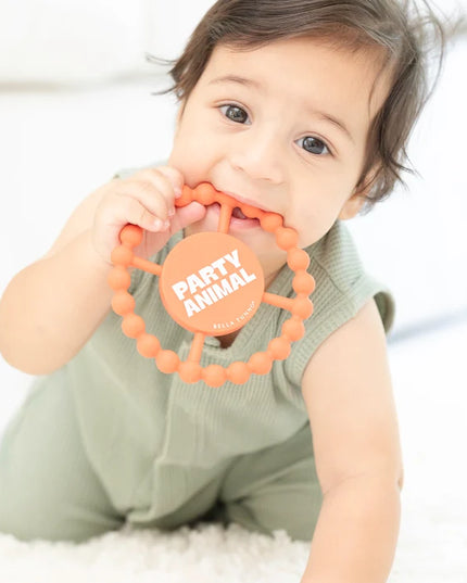 Baby holding orange silicone teething ring with 'party animal text