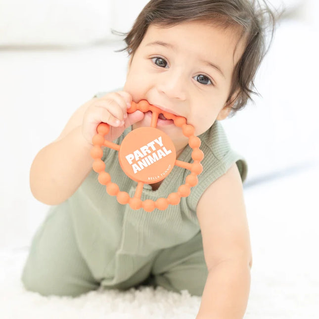 Baby holding orange silicone teething ring with 'party animal text