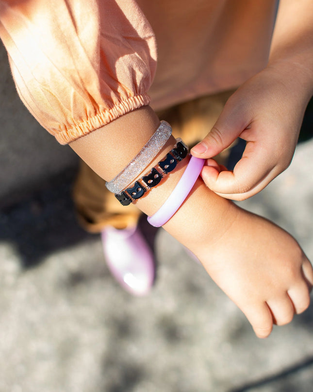 Girl wearing 3 bracelets - one purple, one with black cats, one with silver glitter