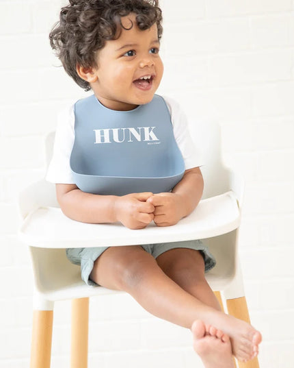Baby wearing blue bib with 'HUNK' printed on it