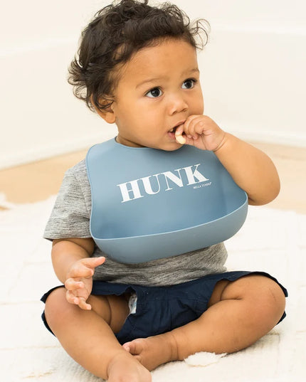 Baby wearing blue bib with 'HUNK' printed on it