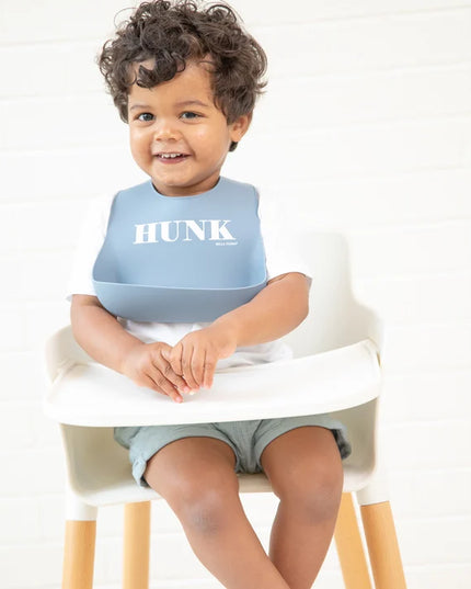 Baby wearing blue bib with 'HUNK' printed on it