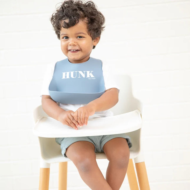 Baby wearing blue bib with 'HUNK' printed on it