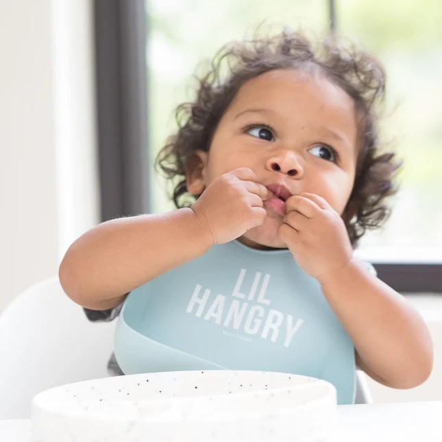 Baby wearing a light blue 'LIL HANGRY' bib while eating.