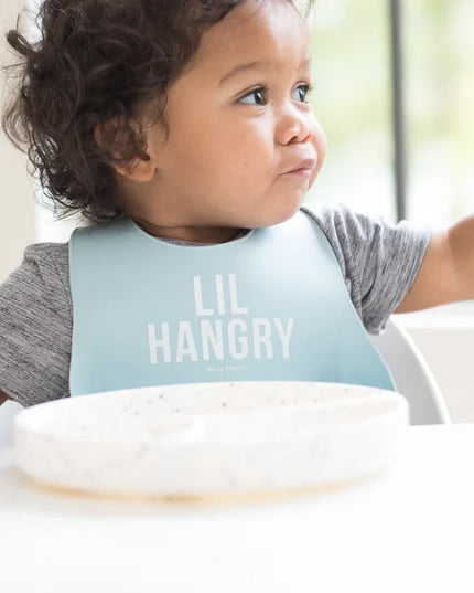 Baby wearing a light blue 'LIL HANGRY' bib while eating.
