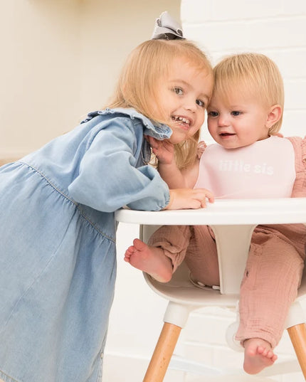 Girl hugging baby wearing a pink baby bib with 'little sis' text 