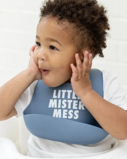 Baby in a high chair wearing blue bib with 'Little Mister Mess' text