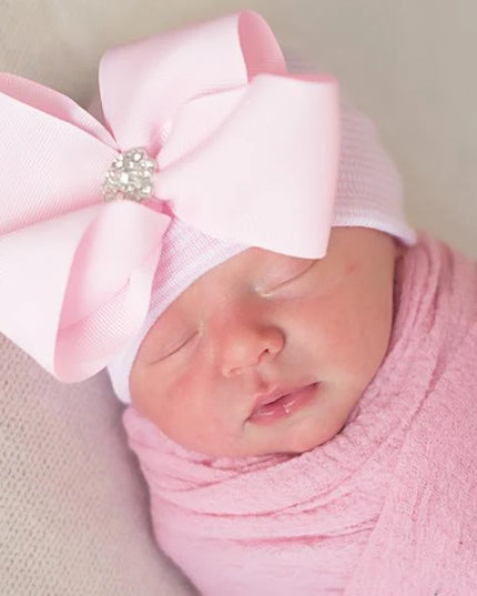 Baby wearing pink and white hospital hat with decorative pink bow 