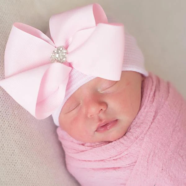 Baby wearing pink and white hospital hat with decorative pink bow 