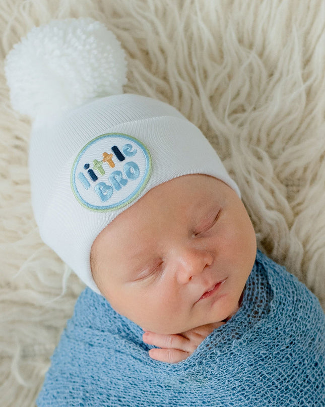 Baby wearing white 'little bro' hospital beanie with pom pom