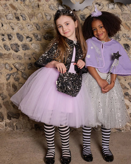 Two young girls in sparkly costumes standing against a stone wall.